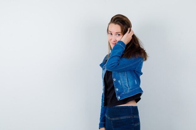 Young lady in blouse, jacket holding hand on head and looking charming , front view.