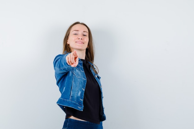 Young lady in blouse, jacket pointing at camera and looking confident , front view.