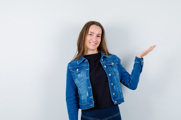 Young lady in blouse, jacket raising spread palm and looking cheerful