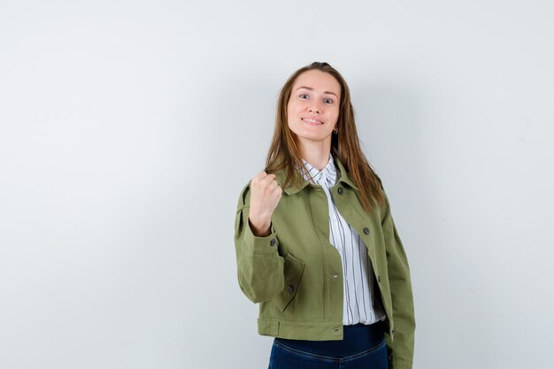 Young lady in blouse, jacket showing winner gesture and looking confident