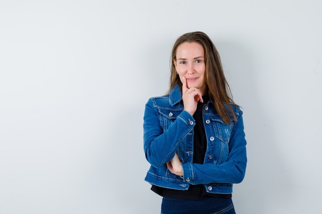 Young lady in blouse, jacket standing in thinking pose and looking confident, front view.