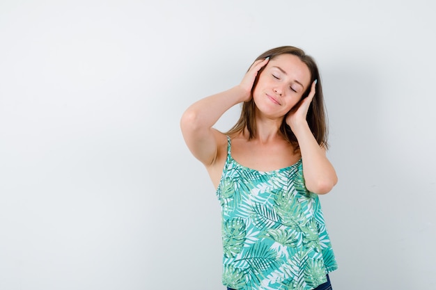 Young lady in blouse massaging head and looking relaxed , front view.