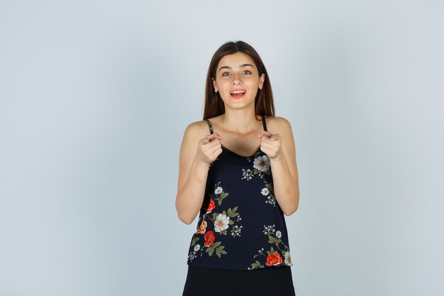 Young lady in blouse pointing at camera and looking happy , front view.