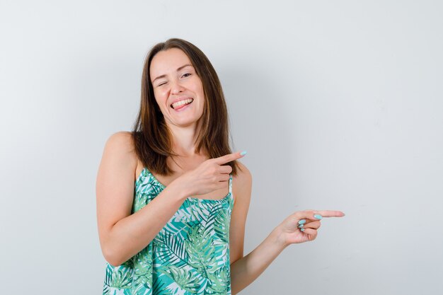 Young lady in blouse pointing to the right side and looking happy , front view.