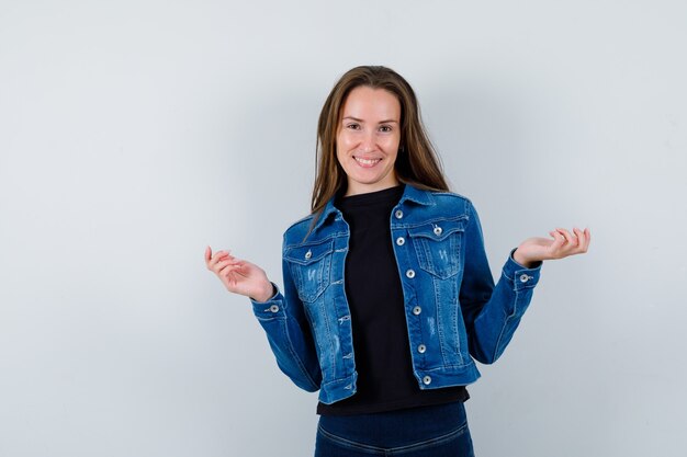 Young lady in blouse posing while spreading palms and looking optimistic , front view.