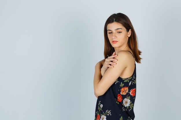 Young lady in blouse posing while touching her arm and looking graceful .