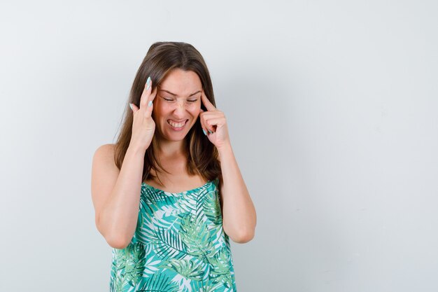 Young lady in blouse rubbing temples and looking exhausted , front view.