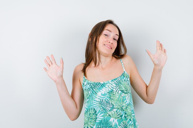 Young lady in blouse showing palms in surrender gesture and looking cute , front view.