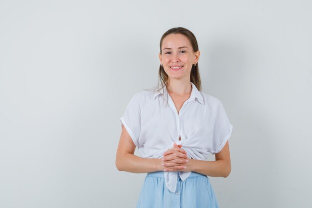 Young lady in blouse and skirt holding hands clasped and looking confident