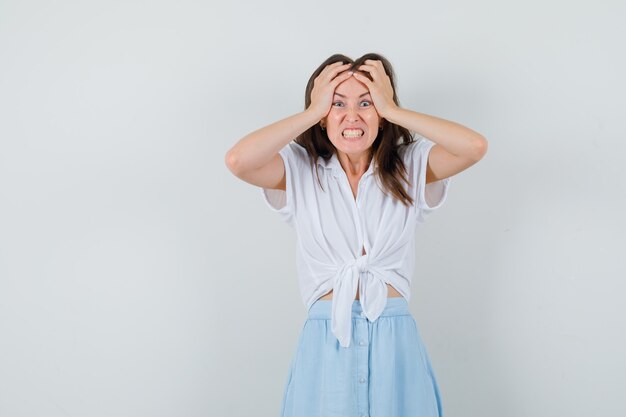 Young lady in blouse, skirt holding hands on her head and looking bored