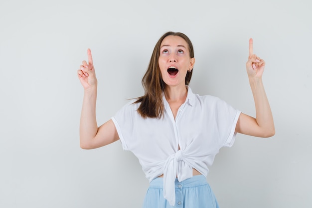 Young lady in blouse and skirt pointing up and looking amazed