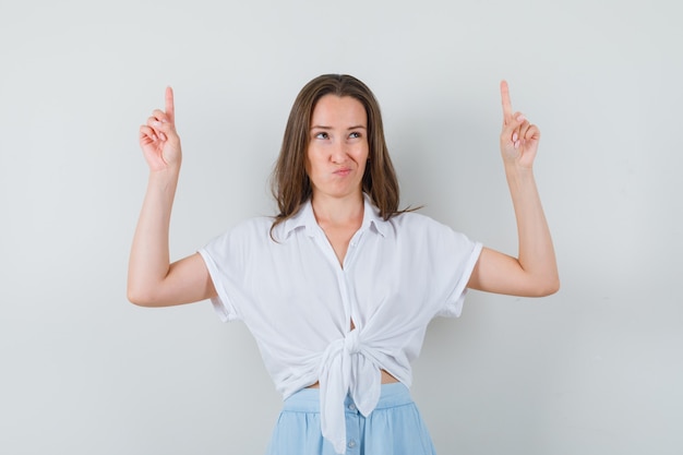 Young lady in blouse and skirt pointing up and looking hesitant