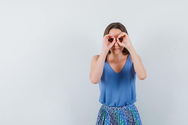 Young lady in blouse,skirt showing binocular gesture and looking concentrated , front view. space for text