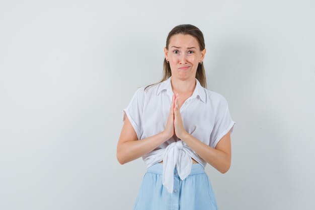 Young lady in blouse and skirt showing namaste gesture and looking doubtful