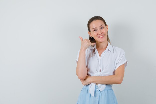 Young lady in blouse and skirt showing phone gesture and looking confident