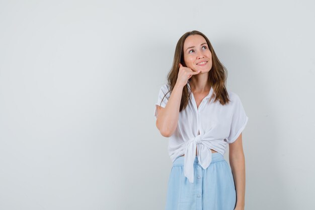 Young lady in blouse and skirt showing phone gesture and looking hopeful