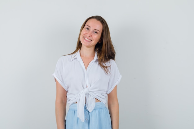 Young lady in blouse, skirt smiling while standing in front of front and looking cute