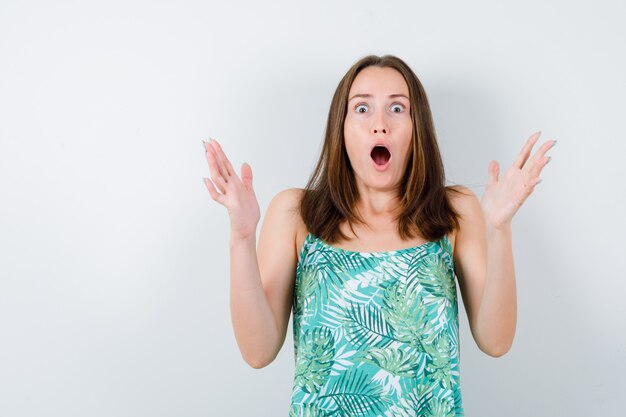 Young lady in blouse standing in scared pose and looking frightened , front view.