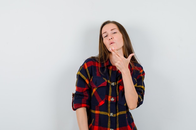 Young lady blowing on finger pistol in casual shirt and looking confident , front view.