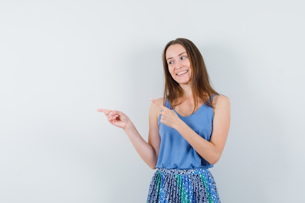 Young lady in blue blouse,skirt pointing aside and looking merry , front view. space for text