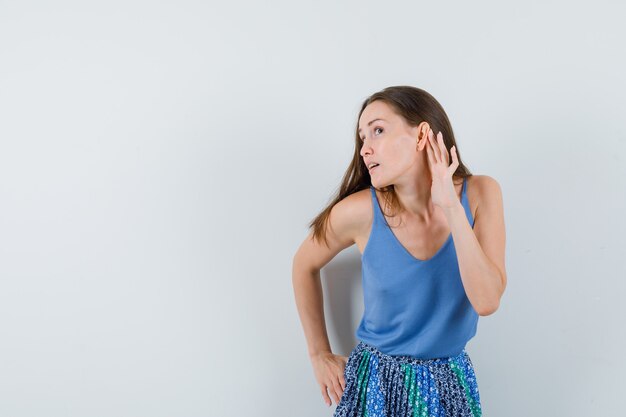 Young lady in blue blouse,skirt trying to listen something and looking attentive , front view.