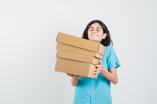 Young lady in blue shirt carrying heavy boxes and looking complicated