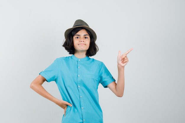 Young lady in blue shirt, hat pointing aside