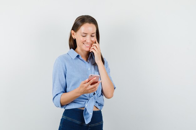 Young lady in blue shirt, pants looking into mobile phone and looking cheerful