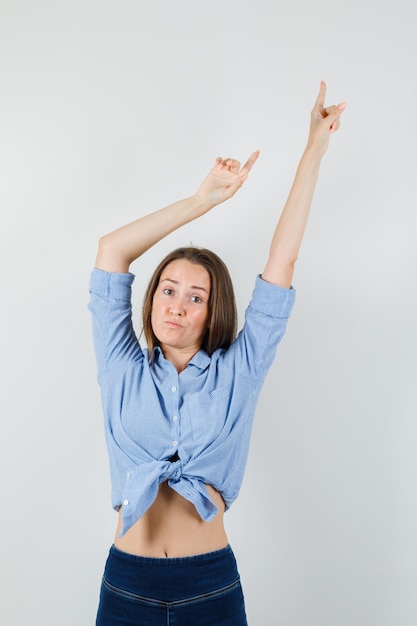 Young lady in blue shirt, pants pointing up by stretching arms and looking disappointed