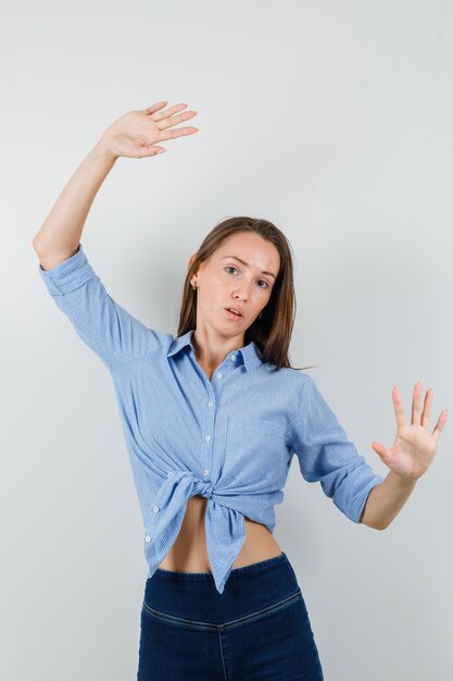 青いシャツを着た若い女性、上げられた手のひらでポーズをとってキュートに見えるパンツ