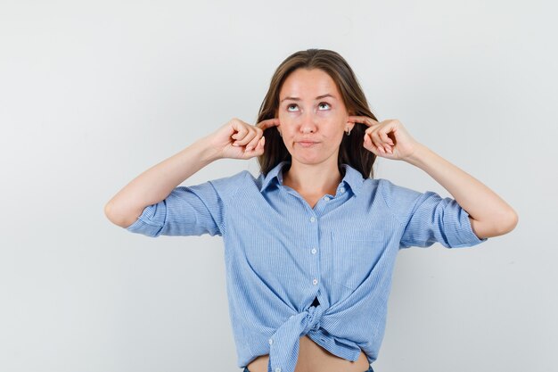 Young lady in blue shirt plugging ears with fingers and looking troubled