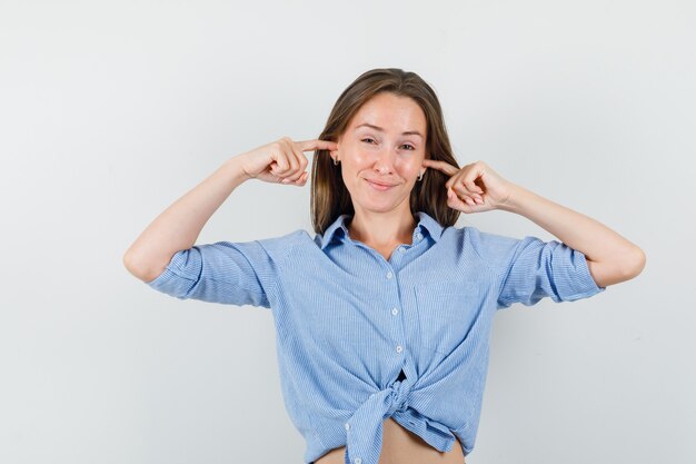 Young lady in blue shirt plugging ears with fingers and looking worried