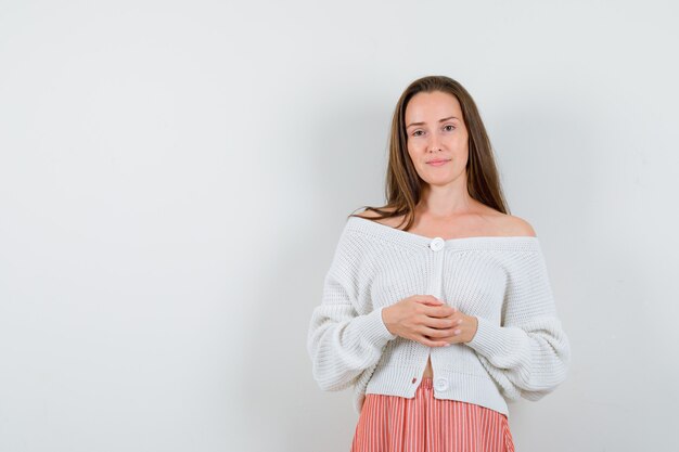 Young lady in cardigan and skirt holding clasped hands isolated