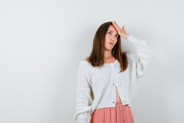 Free photo young lady in cardigan and skirt holding hand on forehead looking forgetfully isolated