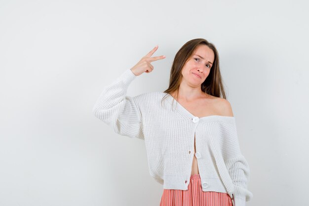 Young lady in cardigan and skirt showing victory sign looking blissful isolated