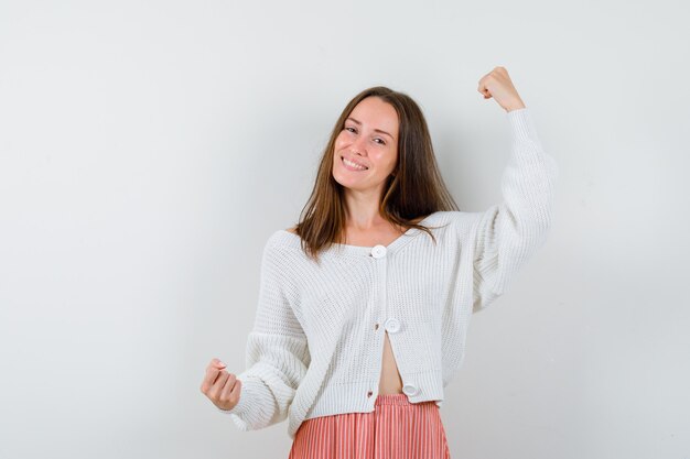 Young lady in cardigan and skirt showing winner gesture looking blissful isolated