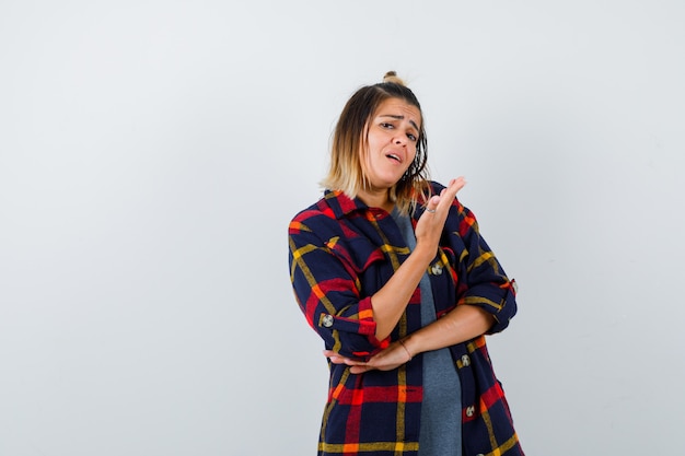 Giovane donna in camicia casual a quadri che tiene il palmo davanti al viso, in piedi di lato e sembra insoddisfatta.