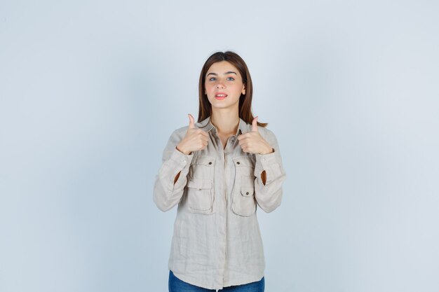 Young lady in casual, jeans showing thumbs up and looking pleased , front view.