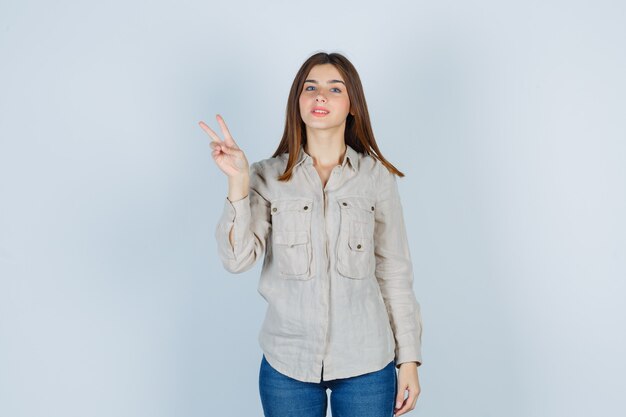 Young lady in casual, jeans showing victory gesture and looking pleased , front view.