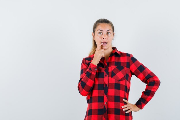 Young lady in casual shirt biting her finger and looking pensive , front view.