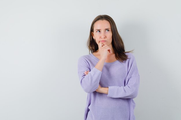 Young lady in casual shirt holding hand on chin and looking pensive 