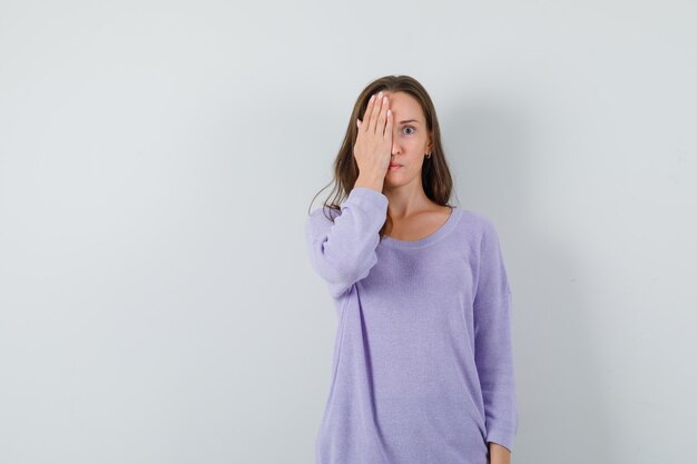 Young lady in casual shirt holding hand on eye and looking curious 