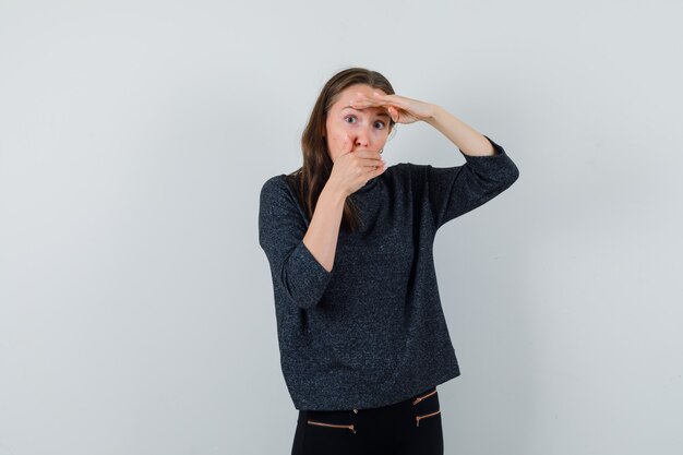 Young lady in casual shirt holding hand on mouth and looking surprised 