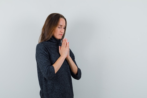 Молодая дама в повседневной рубашке держится за руки в молитвенном жесте и выглядит спокойной