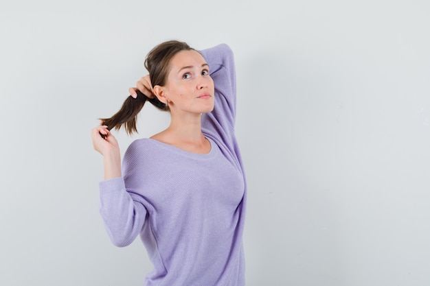 Young lady in casual shirt holding her strand and looking pensive 