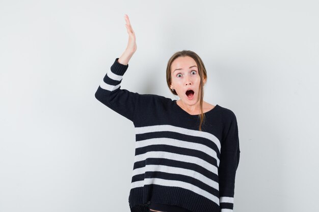 Young lady in casual shirt keeping hand raised and looking wondered