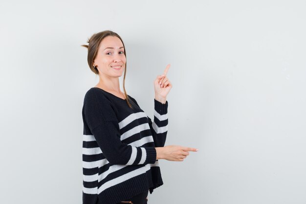 Young lady in casual shirt pointing aside and up and looking cheery