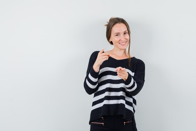 Young lady in casual shirt pointing at front and looking cheery