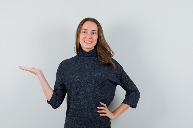 Young lady in casual shirt presenting something and looking cheerful 