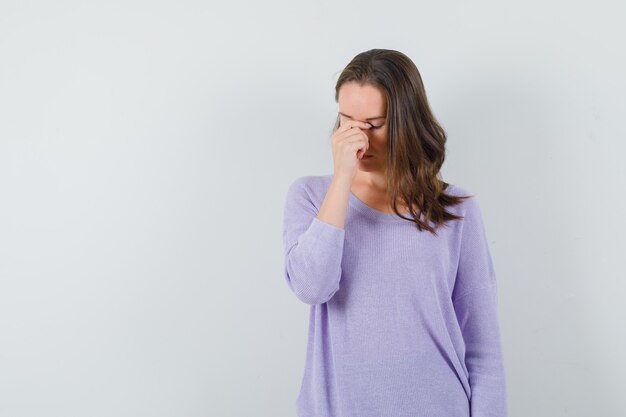 Young lady in casual shirt rubbing eyes and nose and looking tired 